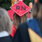 A nursing graduate wearing a red mortarboard with "earned it! 2024" written on it, viewed from behind at a graduation ceremony.
