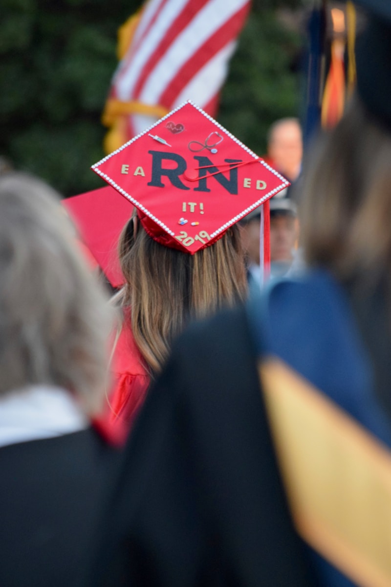 A nursing graduate wearing a red mortarboard with "earned it! 2024" written on it, viewed from behind at a graduation ceremony.